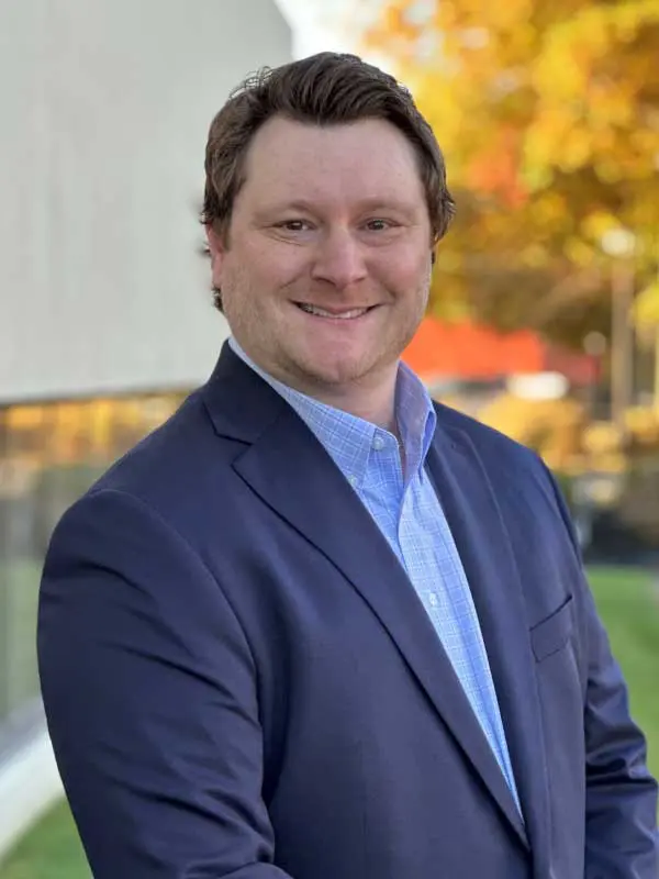 A photo of Chaz Nichols wearing a navy suit with a light blue dress shirt.