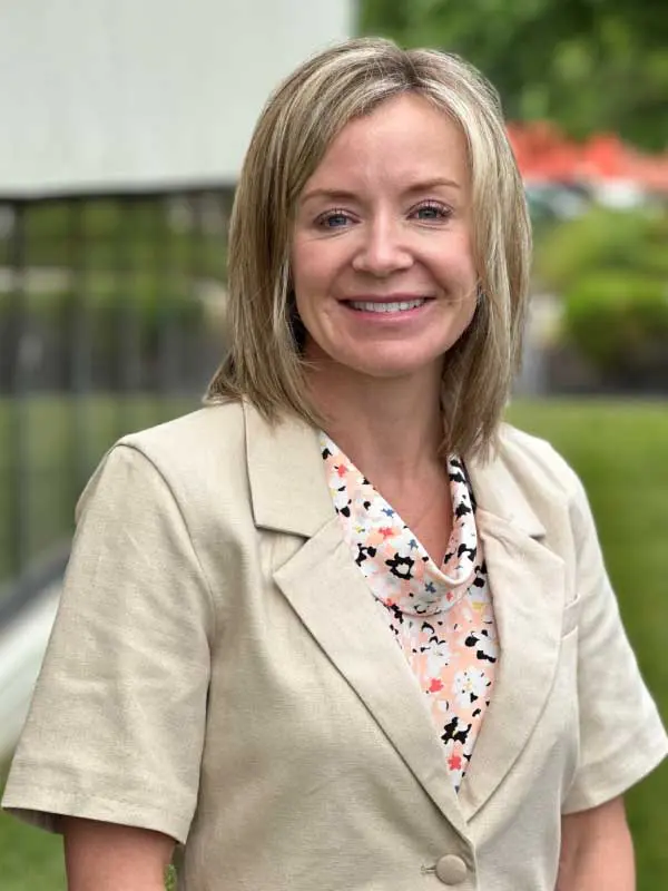 A photo of Kelly Cooley wearing a tan blazer with a floral blouse.